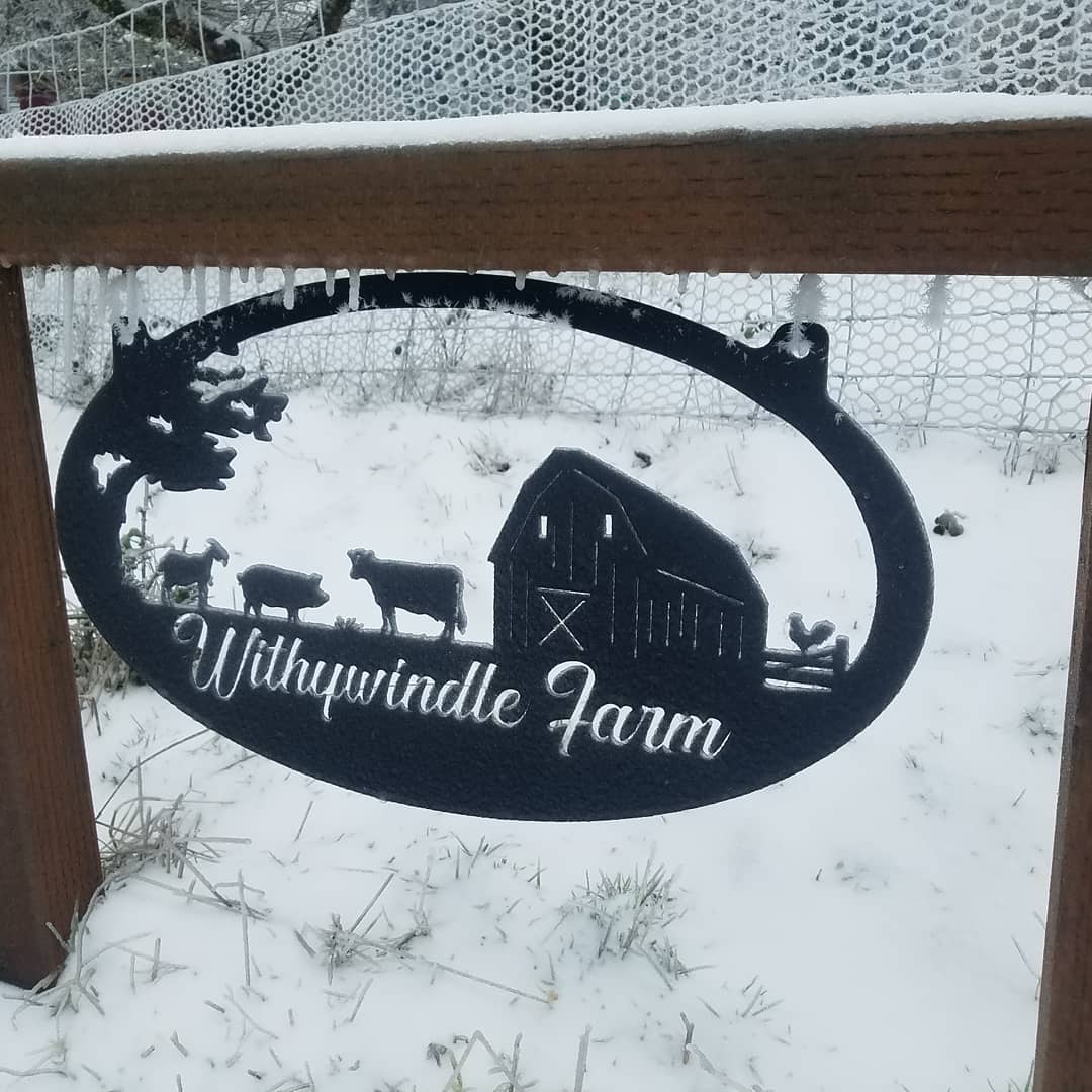 an oval sign made from black metal with the words 'Withywindle Farm' cut into it